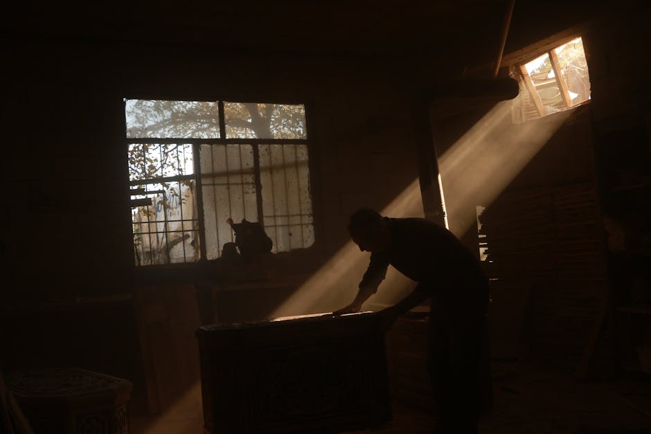 Artistic silhouette of a carpenter working in a sunlit workshop filled with dust and light.