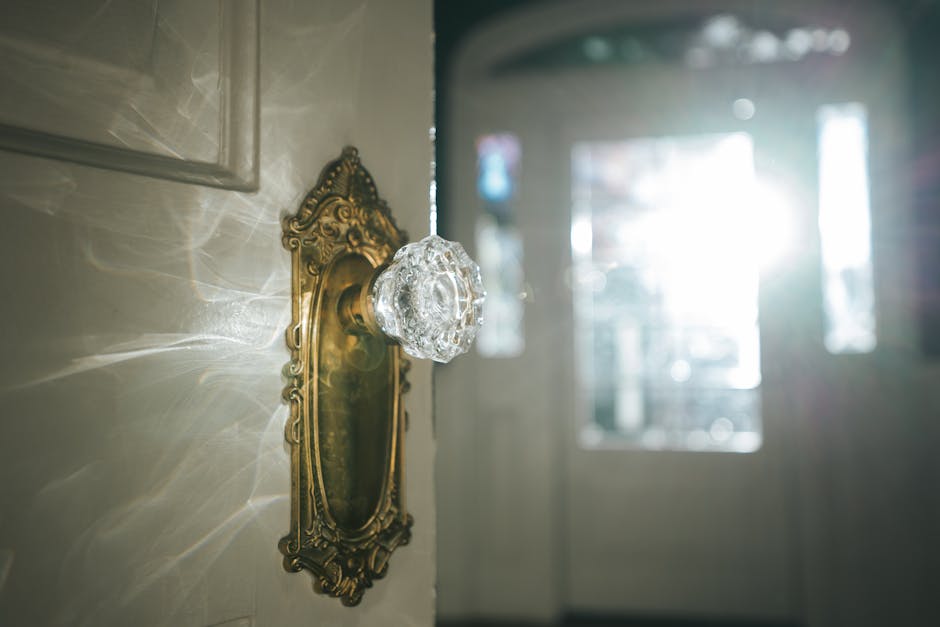 A close-up of an ornate vintage glass door knob with sunlight streaming through an open door.